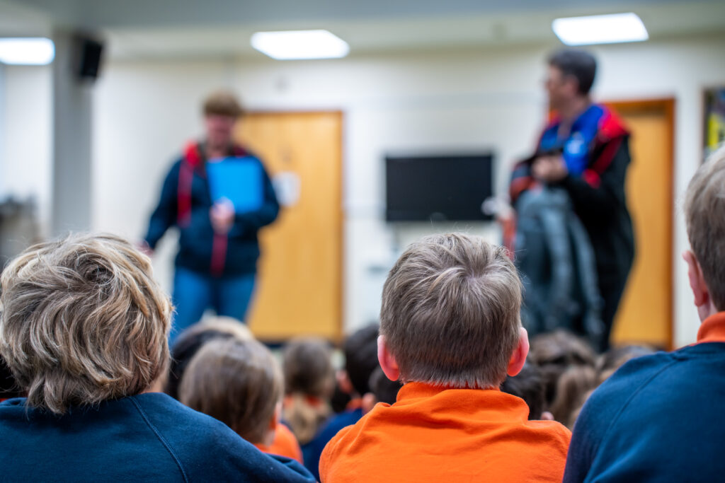 Children sitting on the floor with two adults delivering an assembly from the front